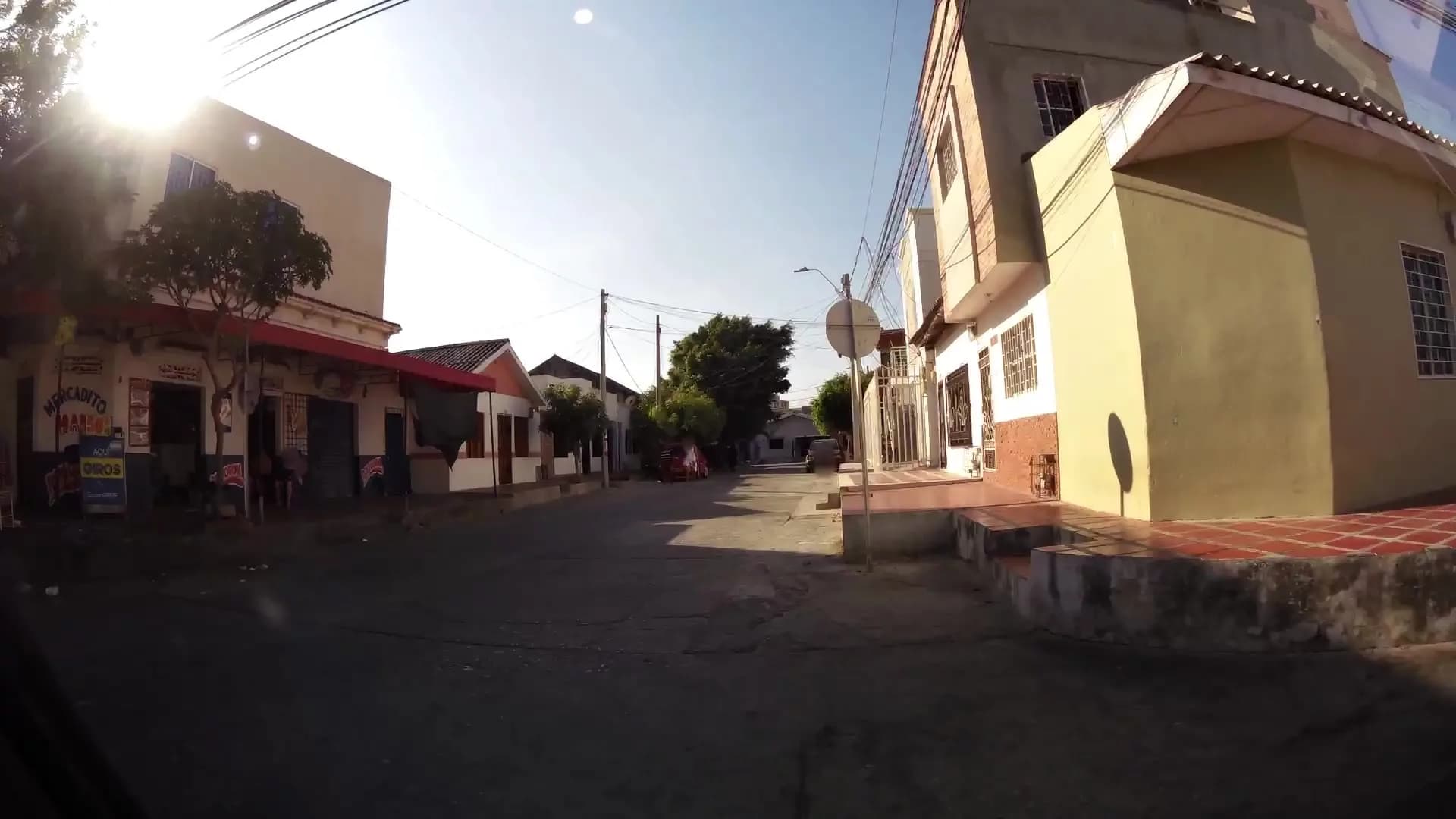 Calle residencial de Barranquilla con una tienda de barrio, árboles, una señal vertical y el pavimento con fisuras